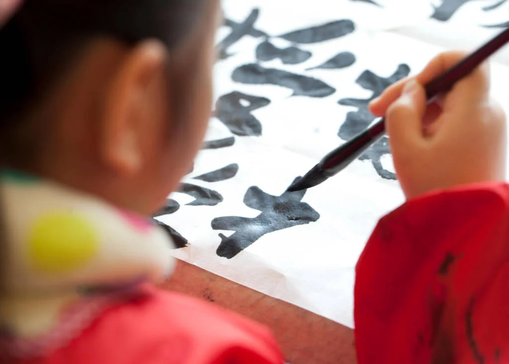 child writing chinese characters with a brush